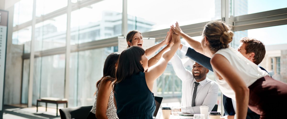 Shot of a group of businesspeople high fiving while sitting in a meeting