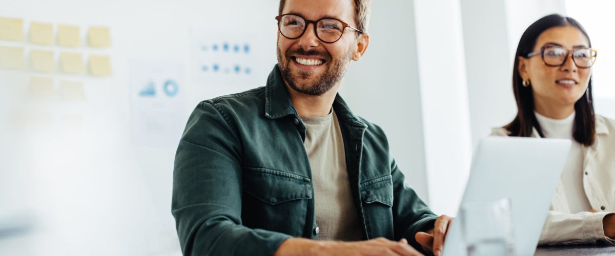 Happy business man listening to a discussion in an office boardroom. Business professional sitting in a meeting with his colleagues.