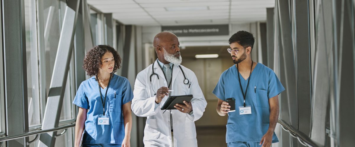 Senior doctor carrying digital tablet, discussing work and walking together with nurses in hospital corridor